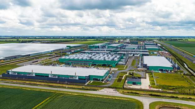 Aerial view of a large industrial data center complex with green buildings and cooling units surrounded by agricultural fields in Middenmeer North Holland Netherlands.