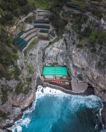Aerial view of turquoise waves crash against rugged cliffs contrasting with the green buildings nestled into the hillside Laurito Campania Italy. Aerial view of turquoise waves crash against rugged cliffs contrasting with the green buildings nestled into the hillside Laurito Campania Italy.