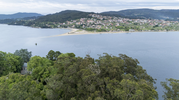 Aerial view of the sandy beach spit and coastal town surrounded by lush green hills and calm waters Cesantes Pontevedra Spain.