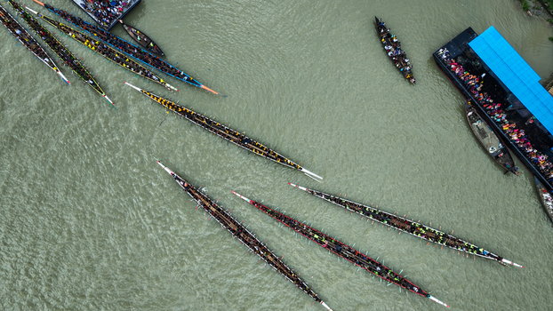 Baghabari Bangladesh 20 August 2022 Aerial view of traditional long boats racing on the river with many rowers and spectators on a large boat.