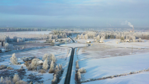 Aerial view of a snowy roundabout surrounded by frost covered trees and rural fields in Latvia. Aerial view of a snowy roundabout surrounded by frost covered trees and rural fields in Latvia.