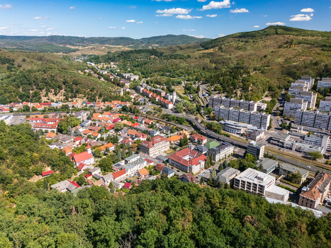Aerial view of Salgotarjan Hungary showing downtown streets rail lines apartment blocks and homes in a green valley beneath surrounding forested hills in summer. Aerial view of Salgotarjan Hungary showing downtown streets rail lines apartment blocks and homes in a green valley beneath surrounding forested hills in summer.