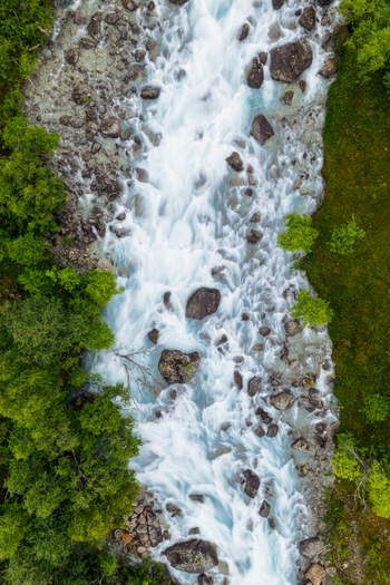 Aerial view of the glacial river in Faueldalen with rushing white water scattered dark rocks and lush green forest banks in Jovik Troms Norway.