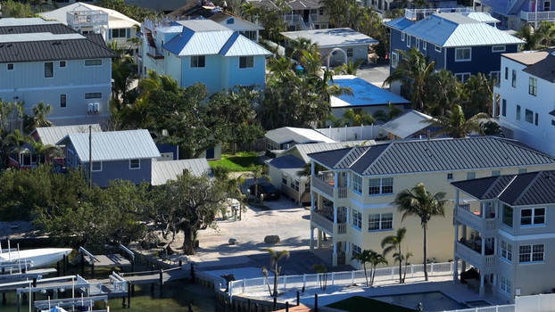 Aerial view of a coastal residential neighborhood featuring multi story houses with metal roofs palm trees and private boat docks in Bradenton Florida United States.