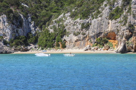View of the turquoise waters and limestone cliffs of the Gulf of Orosei with two motorboats anchored near the sandy beach in Italy. View of the turquoise waters and limestone cliffs of the Gulf of Orosei with two motorboats anchored near the sandy beach in Italy.