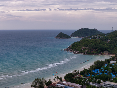Aerial view of Ko Tao featuring turquoise waters sandy beach lush green hills and traditional long tail boats anchored in the bay in Ko Tao Surat Thani Thailand.