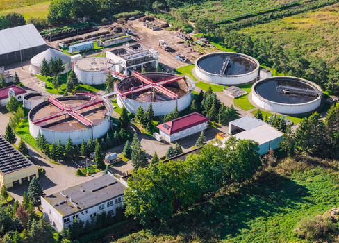 Aerial view of a wastewater treatment plant with circular sedimentation tanks industrial buildings and surrounding green trees in Pomeranian Voivodeship Poland. Aerial view of a wastewater treatment plant with circular sedimentation tanks industrial buildings and surrounding green trees in Pomeranian Voivodeship Poland.