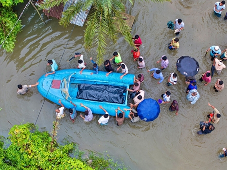 Banshkhali Upazila Chittagong Division Bangladesh 10 July 2026 Aerial view of people wading through floodwaters and guiding a small blue boat carrying a covered body. Banshkhali Upazila Chittagong Division Bangladesh 10 July 2026 Aerial view of people wading through floodwaters and guiding a small blue boat carrying a covered body.