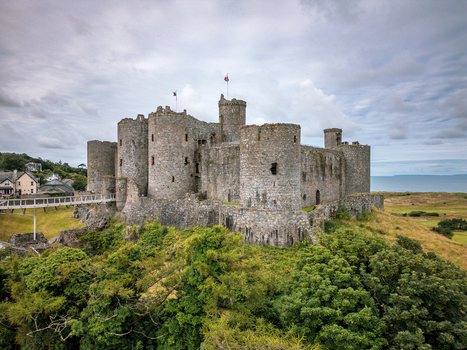 Aerial view of Castell Harlech a medieval stone fortress with massive round towers on a rocky outcrop surrounded by lush green trees Harlech Wales United Kingdom.