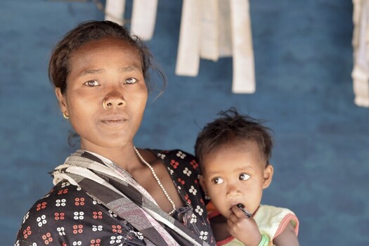 Odisha India 26 March 2026 View of a woman with a child their dark skin contrasting with the bright blue wall showcasing their strong connection. Odisha India 26 March 2026 View of a woman with a child their dark skin contrasting with the bright blue wall showcasing their strong connection.