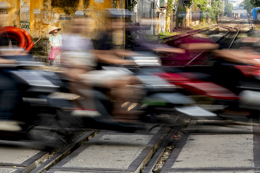 Hanoi Vietnam 11 November 2025 View of a woman wearing a conical hat sitting by the famous Hanoi Train Street as motorbikes speed past in a motion blur.