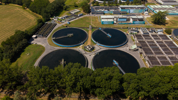 Aerial view of a wastewater treatment plant featuring large circular sedimentation tanks and industrial infrastructure surrounded by lush green trees and fields in Milan Lombardy Italy. Aerial view of a wastewater treatment plant featuring large circular sedimentation tanks and industrial infrastructure surrounded by lush green trees and fields in Milan Lombardy Italy.