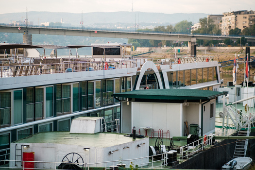 View of a river cruise ship docked on the Danube river with a bridge in the background and city buildings in Novi Sad Vojvodina Serbia. View of a river cruise ship docked on the Danube river with a bridge in the background and city buildings in Novi Sad Vojvodina Serbia.