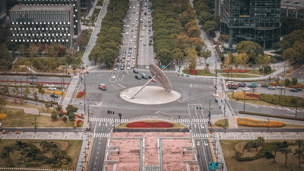 Aerial view of the Century Avenue roundabout featuring a large sculpture surrounded by lush trees modern office buildings and flowing traffic in Shanghai Shanghai China.