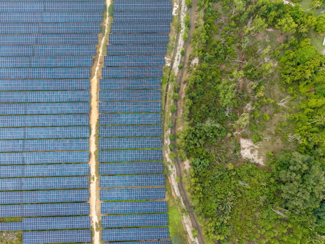 Aerial view of large scale solar photovoltaic power plant with rows of solar panels adjacent to lush green vegetation and a dirt path in Central Seberang Perai Penang Malaysia. Aerial view of large scale solar photovoltaic power plant with rows of solar panels adjacent to lush green vegetation and a dirt path in Central Seberang Perai Penang Malaysia.