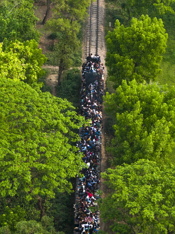 Dhaka Bangladesh 27 March 2026 Aerial view of a train packed with people moving through lush green trees creating a striking contrast between the dark train and vibrant foliage. Dhaka Bangladesh 27 March 2026 Aerial view of a train packed with people moving through lush green trees creating a striking contrast between the dark train and vibrant foliage.