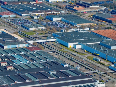 Aerial view of expansive industrial rooftops reflecting the sun interspersed with rows of parked cars and roadways creating a textured urban landscape Sausheim Grand Est France.