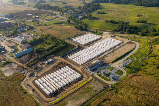 Aerial view of a battery storage facility featuring rows of white containers electrical transformers and switchgear in a rural landscape in Poland.