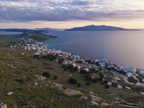 Aerial view of the coastal city of Saranda nestled between rocky hills and the Ionian Sea featuring white buildings and soft sunset light in Saranda Vlore County Albania. Aerial view of the coastal city of Saranda nestled between rocky hills and the Ionian Sea featuring white buildings and soft sunset light in Saranda Vlore County Albania.