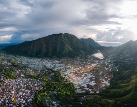 Aerial view of the Sembalun agricultural basin nestled at the foothills of Mount Rinjani with patchwork fields lush greenery and the town of Sembalun West Nusa Tenggara Indonesia. Aerial view of the Sembalun agricultural basin nestled at the foothills of Mount Rinjani with patchwork fields lush greenery and the town of Sembalun West Nusa Tenggara Indonesia.