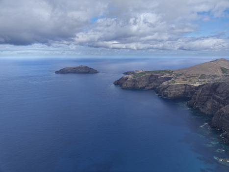 Aerial view of the rugged cliffs of Ponta da Calheta overlooking the deep blue Atlantic Ocean with a distant island under a cloudy sky in Porto Santo Madeira Portugal. Aerial view of the rugged cliffs of Ponta da Calheta overlooking the deep blue Atlantic Ocean with a distant island under a cloudy sky in Porto Santo Madeira Portugal.