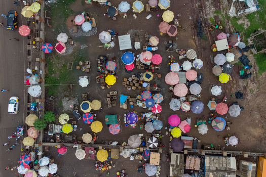 Aerial view of a bustling outdoor market with numerous colorful umbrellas and stalls showing people navigating the busy space in Elmina Central Region Ghana. Aerial view of a bustling outdoor market with numerous colorful umbrellas and stalls showing people navigating the busy space in Elmina Central Region Ghana.