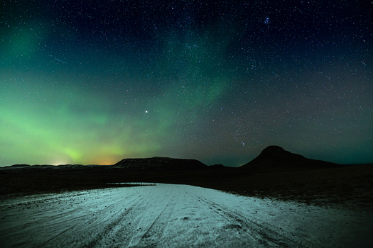 View of an ethereal dance of green and blue hues illuminating the stark snow covered ground under a starlit sky Krysuvikurkirkja Hafnarfjardarkaupstadur Iceland.