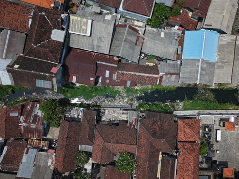 Aerial view of dense residential housing with terracotta rooftops and a narrow canal flowing through the urban landscape in Kecamatan Denpasar Barat Bali Indonesia. Aerial view of dense residential housing with terracotta rooftops and a narrow canal flowing through the urban landscape in Kecamatan Denpasar Barat Bali Indonesia.