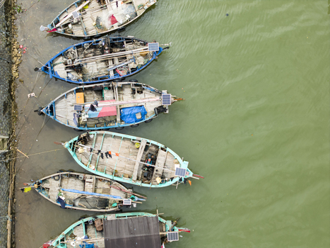 Aerial view of weathered fishing boats their teal and blue paint peeling under the harsh sun resting beside a muddy shore Jepara Central Java Indonesia.