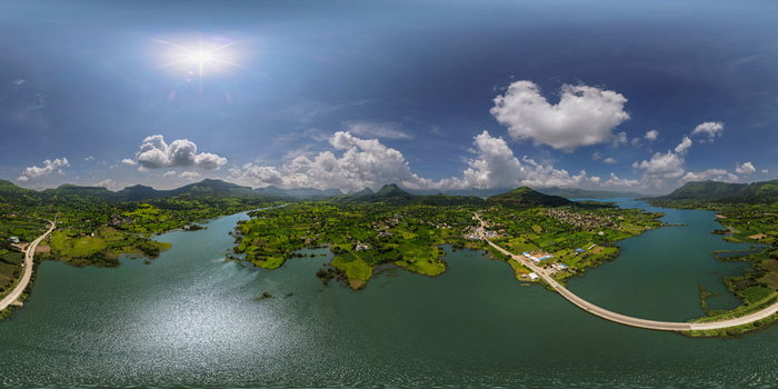 Aerial view of a serene lake surrounded by lush green hills and a winding road under a bright blue sky in Maharashtra India. Aerial view of a serene lake surrounded by lush green hills and a winding road under a bright blue sky in Maharashtra India.