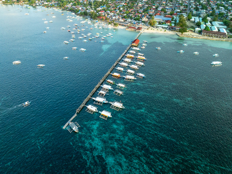 Aerial view of a long wooden pier with traditional outrigger boats moored in clear turquoise water near the coast of Siargao Philippines. Aerial view of a long wooden pier with traditional outrigger boats moored in clear turquoise water near the coast of Siargao Philippines.