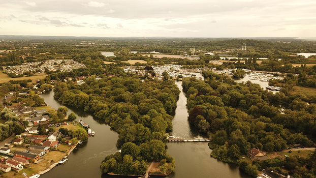 Aerial view of the Thames River winding through lush green trees residential areas and small boat moorings in the United Kingdom. Aerial view of the Thames River winding through lush green trees residential areas and small boat moorings in the United Kingdom.