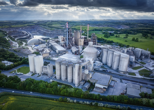 Aerial view of the Irish Cement Ltd industrial facility featuring large silos and chimneys surrounded by green fields and a quarry under a dramatic sky in Drogheda County Louth Ireland. Aerial view of the Irish Cement Ltd industrial facility featuring large silos and chimneys surrounded by green fields and a quarry under a dramatic sky in Drogheda County Louth Ireland.