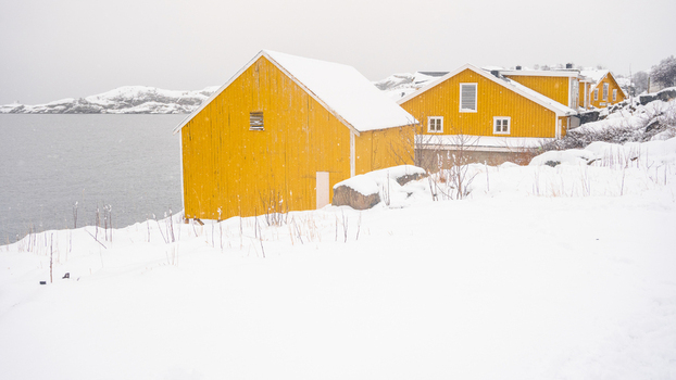 View of traditional yellow wooden cabins situated on a snowy coastline by the sea in Leknes Lofoten Norway.