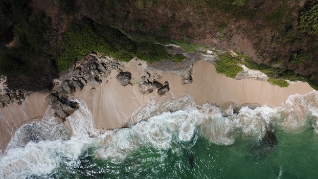 Aerial view of a secluded beach with rocky cliffs white sand and turquoise ocean waves crashing against the shore in Indonesia.
