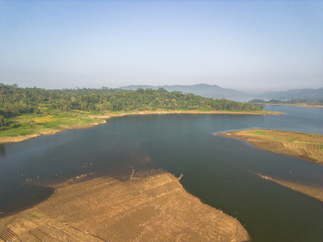 Aerial view of Wadaslintang Reservoir surrounded by lush green hills agricultural fields and calm water under a clear blue sky in Wadaslintang Central Java Indonesia. Aerial view of Wadaslintang Reservoir surrounded by lush green hills agricultural fields and calm water under a clear blue sky in Wadaslintang Central Java Indonesia.