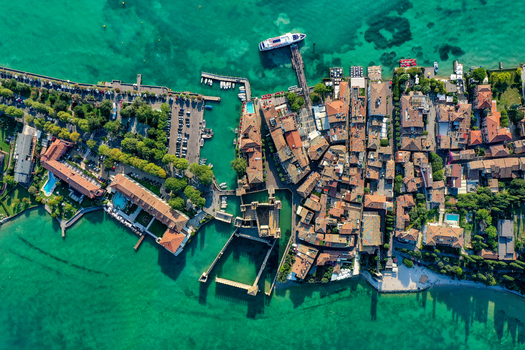 Aerial view of Scaligero Castle and the historic town of Sirmione on the shores of Lake Garda with turquoise waters boats and a parking lot Italy. Aerial view of Scaligero Castle and the historic town of Sirmione on the shores of Lake Garda with turquoise waters boats and a parking lot Italy.