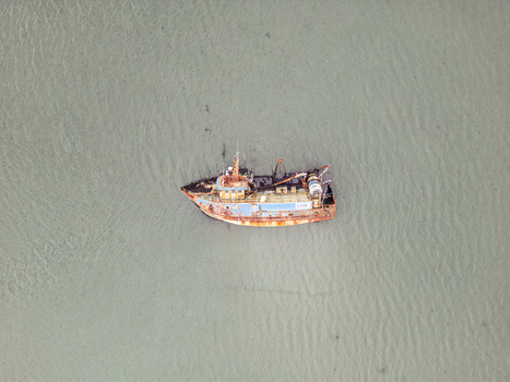 Aerial view of a rusty abandoned fishing boat floating in calm murky water with a weathered hull and deck equipment. Aerial view of a rusty abandoned fishing boat floating in calm murky water with a weathered hull and deck equipment.