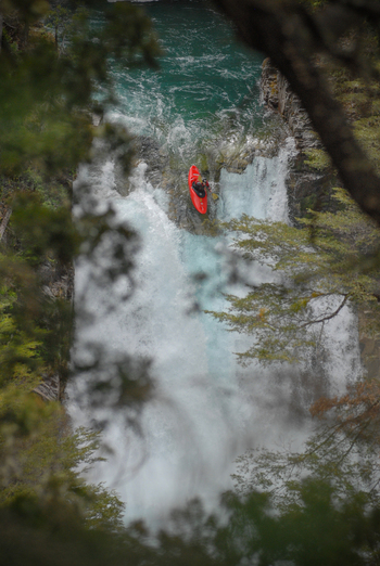 View of a kayaker in a red kayak navigating the white water of a waterfall on the Rio Manso surrounded by lush trees in San Carlos de Bariloche Rio Negro Argentina. View of a kayaker in a red kayak navigating the white water of a waterfall on the Rio Manso surrounded by lush trees in San Carlos de Bariloche Rio Negro Argentina.