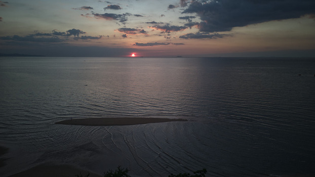 Aerial view of Jomtien Beach at sunset with the sun dipping below the horizon over the calm sea and a small sandbar in the foreground Chon Buri Thailand.