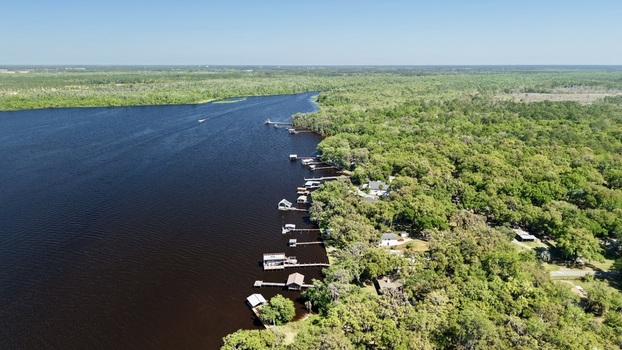 Aerial view of Sixmile Creek with wooden docks and boathouses along the lush green forested shoreline under a clear blue sky St. Johns County Florida United States.