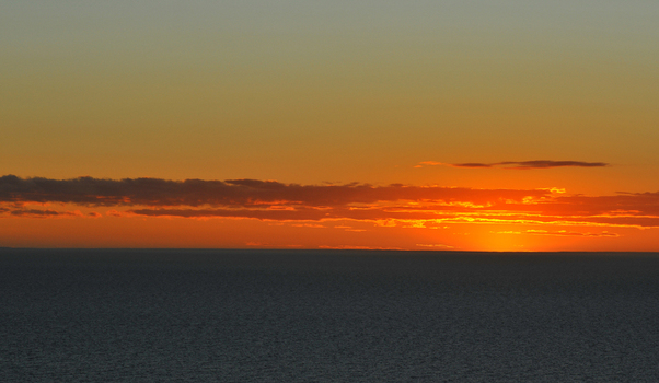 View of the vibrant sunset over the calm Atlantic Ocean with orange clouds on the horizon at Puerto Piramides Puerto Madryn Chubut Argentina. View of the vibrant sunset over the calm Atlantic Ocean with orange clouds on the horizon at Puerto Piramides Puerto Madryn Chubut Argentina.