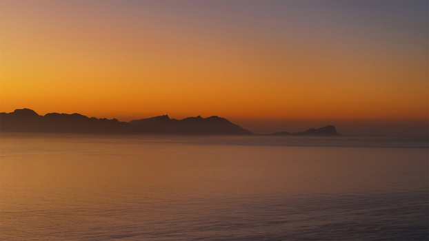 Aerial view of the silhouetted mountain range across the calm ocean waters under a vibrant orange and purple sunset sky in Cape Town Western Cape South Africa. Aerial view of the silhouetted mountain range across the calm ocean waters under a vibrant orange and purple sunset sky in Cape Town Western Cape South Africa.