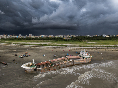 Chattogram Bangladesh 22 September 2026 Aerial view of a large beached cargo ship on the sandy shore with small fishing boats people walking and a dramatic stormy sky over the city.