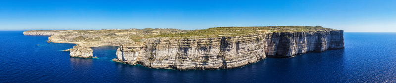 Aerial view of the high limestone cliffs and rugged coastline of Dwejra Bay overlooking the deep blue Mediterranean Sea in Gozo Region Malta. Aerial view of the high limestone cliffs and rugged coastline of Dwejra Bay overlooking the deep blue Mediterranean Sea in Gozo Region Malta.
