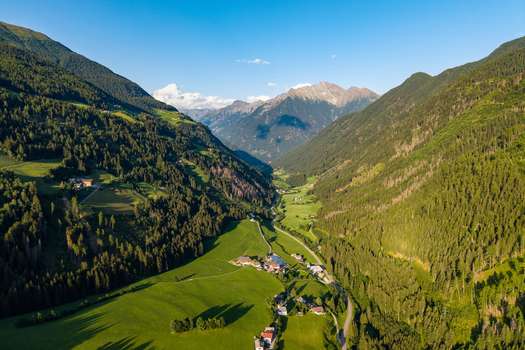 Aerial view of the lush green valley of Muhlwald with dense pine forests scattered farmhouses and rolling meadows nestled between high mountains in Muhlwald Trentino Alto Adige Italy. Aerial view of the lush green valley of Muhlwald with dense pine forests scattered farmhouses and rolling meadows nestled between high mountains in Muhlwald Trentino Alto Adige Italy.
