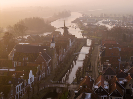 Aerial view of the historic town of Sloten featuring traditional gabled houses a classic windmill and a calm canal under a soft morning mist in Sloten Friesland Netherlands. Aerial view of the historic town of Sloten featuring traditional gabled houses a classic windmill and a calm canal under a soft morning mist in Sloten Friesland Netherlands.