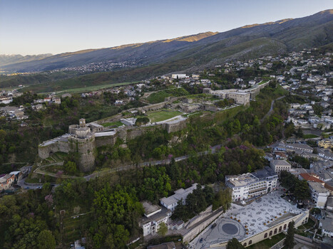 Aerial view of Gjirokaster Fortress a historic stone castle overlooking the city with surrounding green hills traditional houses and a paved square Gjirokaster Gjirokaster County Albania. Aerial view of Gjirokaster Fortress a historic stone castle overlooking the city with surrounding green hills traditional houses and a paved square Gjirokaster Gjirokaster County Albania.