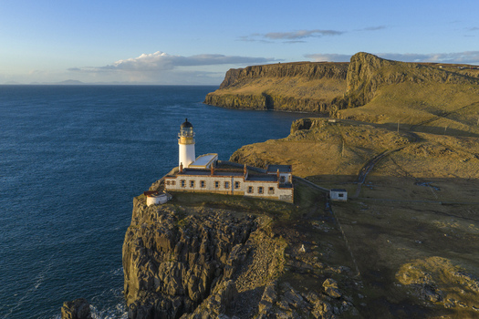 Aerial view of Neist Point Lighthouse on a rugged cliff edge overlooking the blue sea during golden hour in Isle of Skye Scotland United Kingdom. Aerial view of Neist Point Lighthouse on a rugged cliff edge overlooking the blue sea during golden hour in Isle of Skye Scotland United Kingdom.