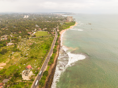 Aerial view of Dadalla beach with waves crashing on the shore a coastal road with traffic and lush greenery near the cemetery in Galle Southern Province Sri Lanka. Aerial view of Dadalla beach with waves crashing on the shore a coastal road with traffic and lush greenery near the cemetery in Galle Southern Province Sri Lanka.